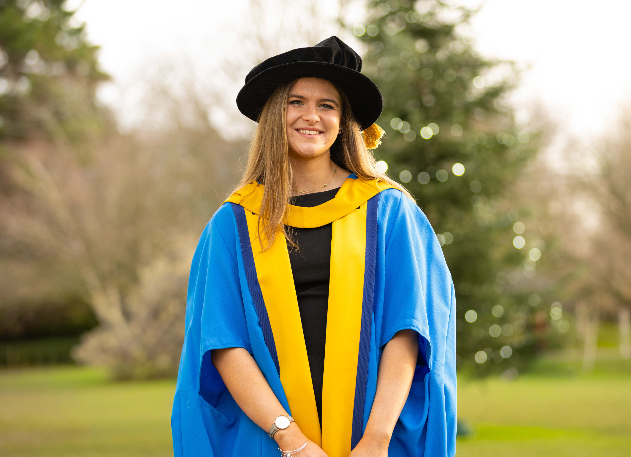 UCD alumna Amber Barry wearing graduation cap and gown, posing for a photo by the main UCD lake.